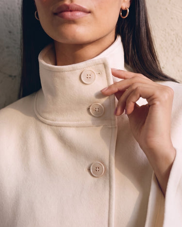 The Lorenne cape coat in white — close-up of the buttoned stand collar