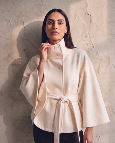 The Lorenne cape coat in white — on model with hand at the stand collar