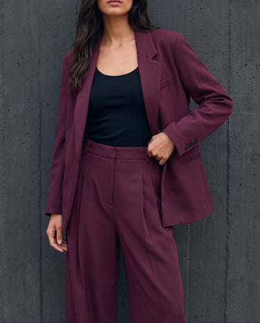 The Aliya Burgundy Blazer Set in burgundy — blazer and trousers, front view with hand in pocket on model