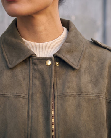 Close-up of the Astor bomber's spread collar, gold snap and faux suede texture in olive green