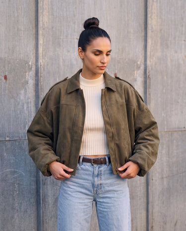 Model with hands in pockets wearing the olive green Astor faux suede bomber, front view