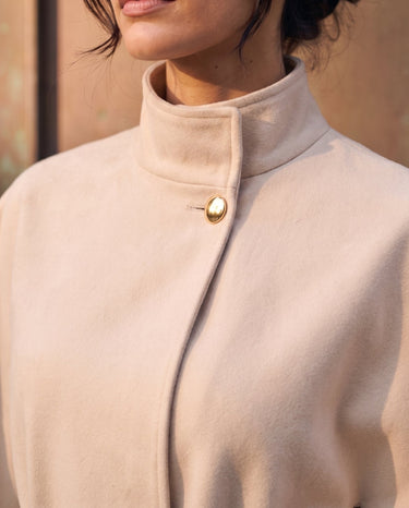 The Aurelia Shawl in beige — close-up of the stand collar and gold button