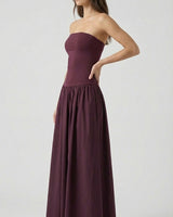 A woman poses confidently with one hand on her hip, wearing the Tamsin Strapless Dress featuring a fitted bodice and gathered skirt, set against a plain light background.