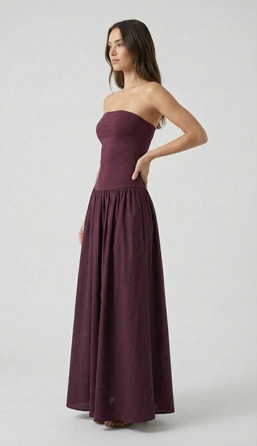 A woman poses confidently with one hand on her hip, wearing the Tamsin Strapless Dress featuring a fitted bodice and gathered skirt, set against a plain light background.