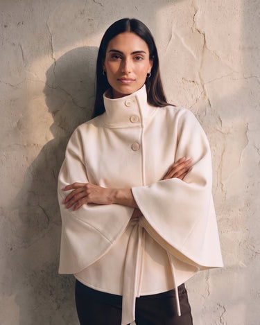 The Lorenne cape coat in white — front view on model with arms crossed