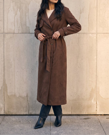 Model tying the belt of the brown Bexley Trench Coat, front view showing the ankle-length hem