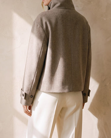 Back view of the Ottilie Funnel Jacket in taupe with standing funnel collar and boxy cropped hem