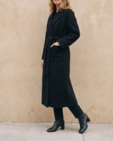 The Caroline Tie Waist Coat in black — longline belted coat, front view with hand in pocket on model