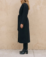 The Caroline Tie Waist Coat in black — longline belted coat, side view on model