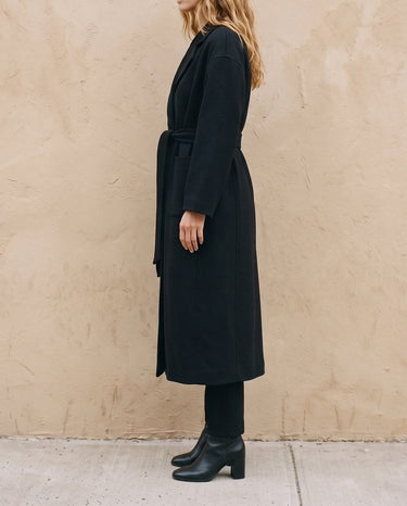 The Caroline Tie Waist Coat in black — longline belted coat, side view on model