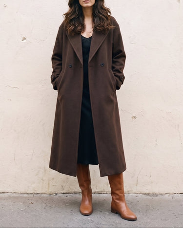 The Chocolate Maxi Coat in chocolate brown — longline coat, front view with hands in pockets on model