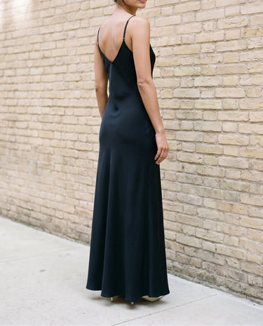 Back three-quarter view of the black Eclipse Satin Dress showing the open back and the drape across the shoulders