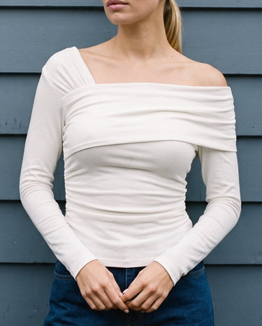 Close front view of the white asymmetric shoulder top worn with jeans – Moriel Heritage