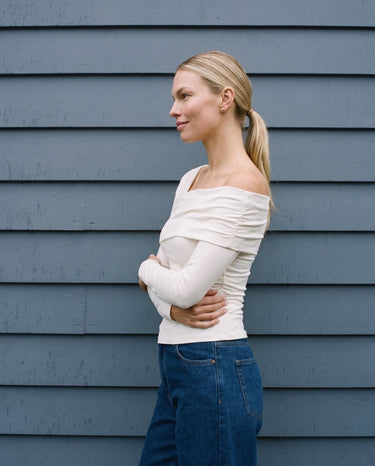 Model with arms crossed in the white asymmetric shoulder top, side view – Moriel Heritage