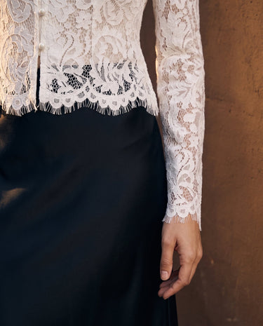 Florence Blouse in white — cropped view of the scalloped lace hem over a black skirt