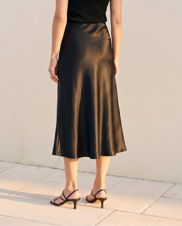 Model wearing black satin midi skirt, back view showing flared hem – Moriel Heritage