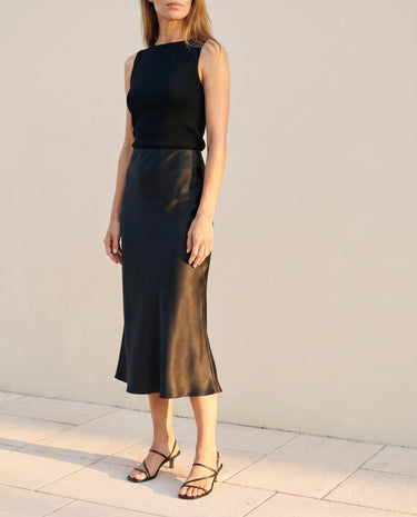 Model wearing black satin midi skirt, full-length side view – Moriel Heritage