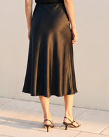 Model wearing black satin midi skirt, cropped back view with strappy heels – Moriel Heritage