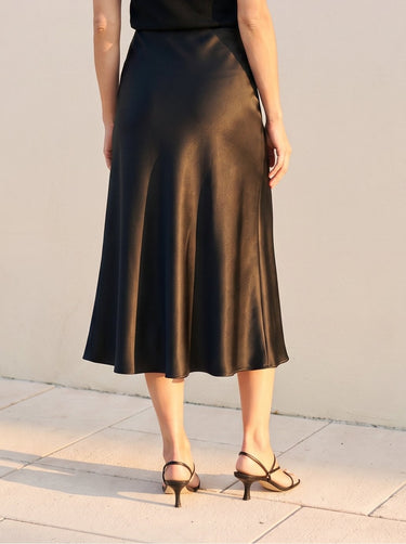 Model wearing black satin midi skirt, cropped back view with strappy heels – Moriel Heritage