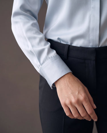 Detail of the light blue satin-look shirt's buttoned cuff over black trousers
