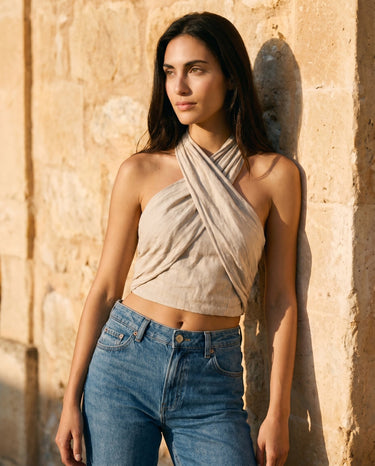 Model in the beige linen crossover halter top beside a stone wall, angled front view – Moriel Heritage