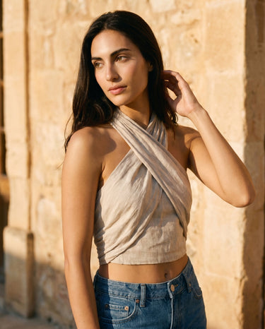 Three-quarter view of the beige linen crossover halter crop top worn with high-waist jeans – Moriel Heritage