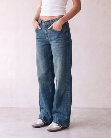 Harlow Low Rise Jeans in washed blue — three-quarter view on model, hands in pockets