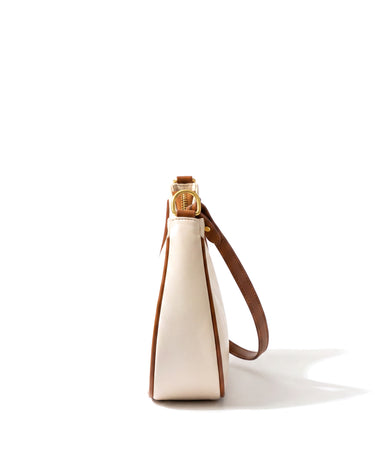 The Ines Crescent Bag in cream with tan trim, side profile view showing the slim depth