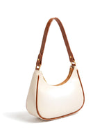 The Ines Crescent Bag in cream with tan trim, three-quarter rear view showing the strap keeper