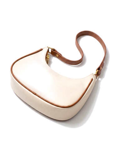 The Ines Crescent Bag in cream with tan trim, elevated view showing the curved top line and strap