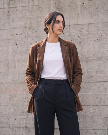 Model standing with hands in pockets wearing the dark brown Isla Faux Suede Jacket, front view