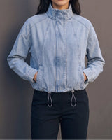 Marbella Denim Jacket — cropped light-wash denim jacket, front view on model with hands in pockets