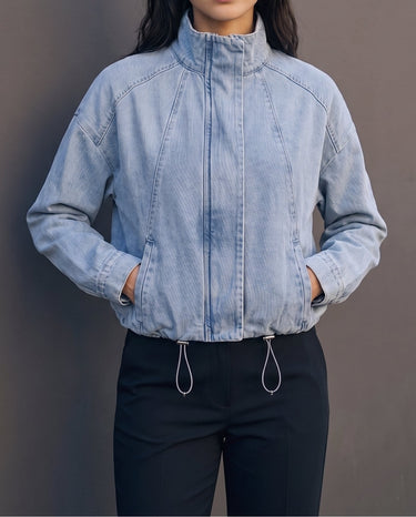 Marbella Denim Jacket — cropped light-wash denim jacket, front view on model with hands in pockets