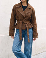 Model wearing the dark brown Margot Tie-waist Coat tied at the waist, front view against a stone wall