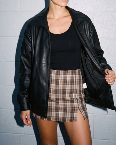 Model holding open the black Marseille Faux Leather Jacket, front view over a black top and check mini skirt