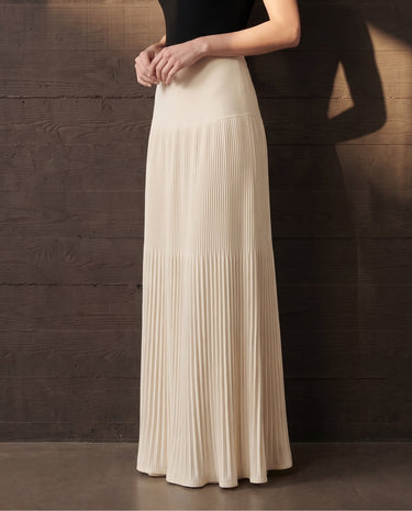 Three-quarter view of the ivory Matilde Skirt showing the pleated maxi skirt in profile with the model's hand at the waist
