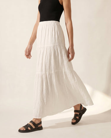 The Noemi A-Line Skirt in white — tiered maxi skirt, side walking view on model