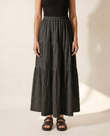 The Noemi A-Line Skirt in black — tiered maxi skirt, front view on model