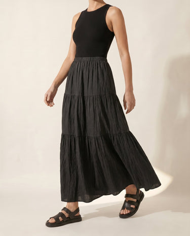 The Noemi A-Line Skirt in black — tiered maxi skirt, side view on model