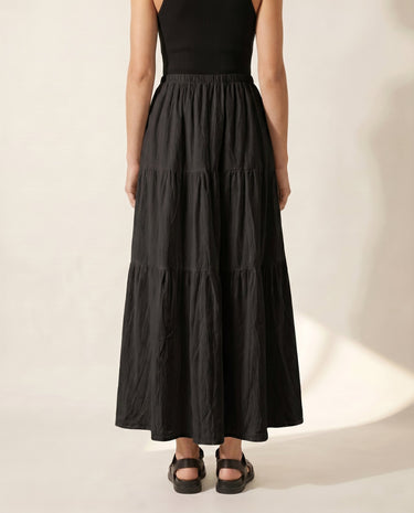 The Noemi A-Line Skirt in black — tiered maxi skirt, front view on model