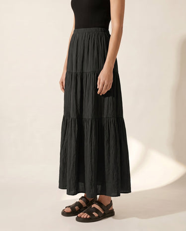 The Noemi A-Line Skirt in black — tiered maxi skirt, side view on model