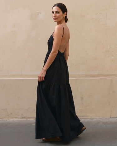 Norah Backless Sling Dress in black — tiered maxi dress showing open back, side view on model