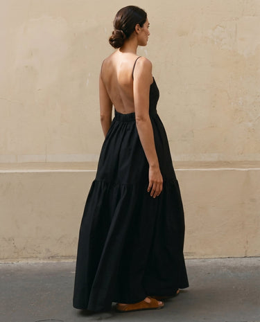 Norah Backless Sling Dress in black — backless tiered maxi dress, back three-quarter view on model