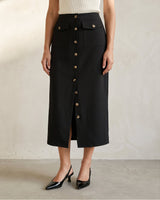 Model wearing the black Elegant Retro Slimming Skirt, front view showing the button placket running the full length and the straight midi cut, styled with a cream knit tank