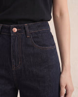 Close-up of dark denim jeans showing high-rise waistband, copper button and contrast topstitching – Moriel Heritage