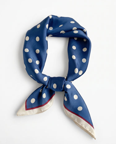 Satin Scarf in navy polka dot — silky square scarf with cream border, tied in a knot, flat lay on white