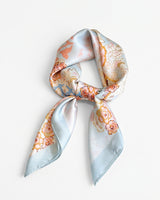 Satin Scarf in powder blue floral — pale blue silky scarf with peach and gold florals, tied, flat lay on white
