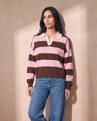 Striped Knit Polo Sweater in pink and cocoa — model leaning on sunlit plaster wall, relaxed styling