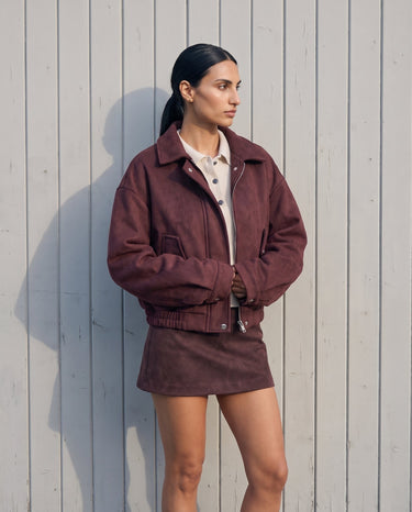 Model in the burgundy suede-look bomber jacket, full-length front view against a white wall