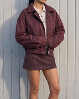 Model in the burgundy suede-look bomber jacket, full-length front view against a white wall